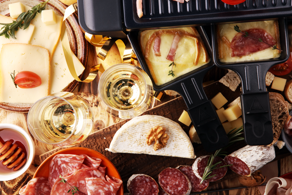 A hot raclette grill with its name-worthy raclette cheese is served with various types of meat, vegetables, and fresh bread.