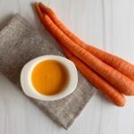 Napkin with white ramakin filled with creamy orange ginger miso salad dressing and 3 carrots on the side.