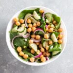 Artfully display white bowl with baby spinach, sliced red onion and chickpeas.
