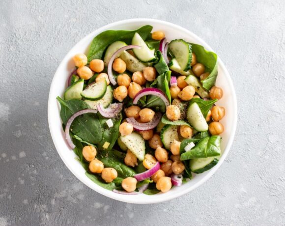 Artfully display white bowl with baby spinach, sliced red onion and chickpeas.