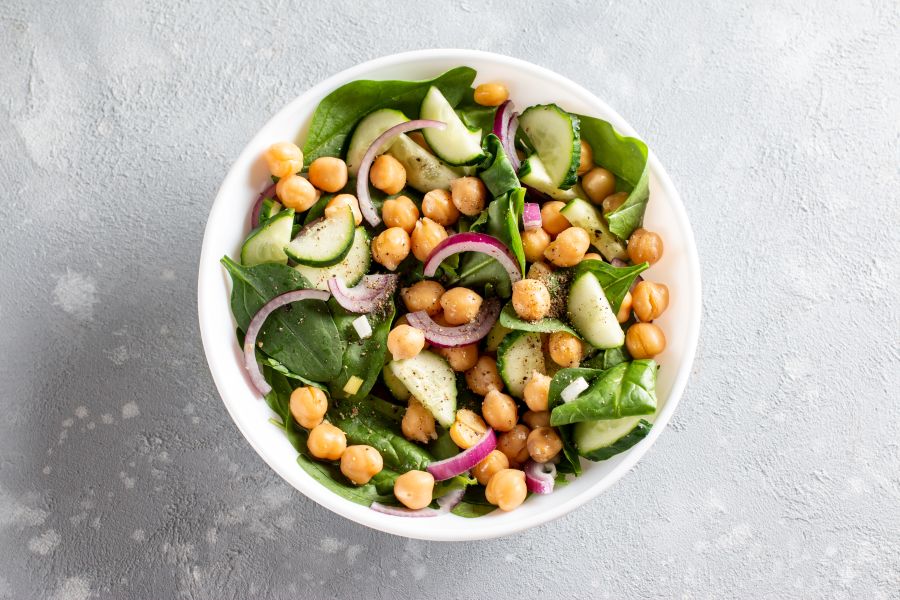Artfully display white bowl with baby spinach, sliced red onion and chickpeas.