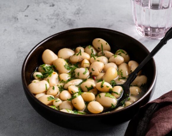 White beans garnished with fresh herbs in a black bowl on a gray background