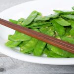 Snow peas sauteed with ginger served on a white plate with chopsticks