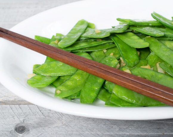Snow peas sauteed with ginger served on a white plate with chopsticks