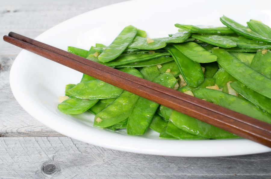 Snow peas sauteed with ginger served on a white plate with chopsticks