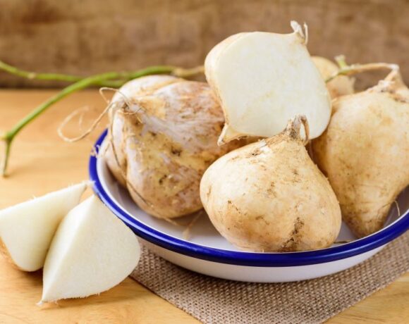 White and blue bowl filled with fresh jicama on a wood table.