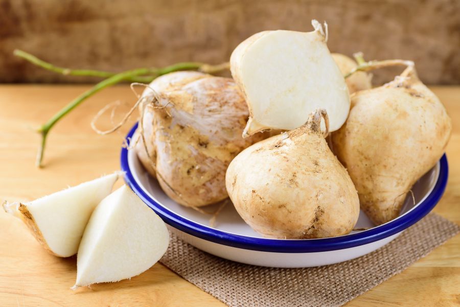 White and blue bowl filled with fresh jicama on a wood table.