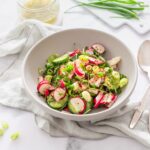 White bowl on a white background filled with a salad composed of radish, cucumber and green onions.