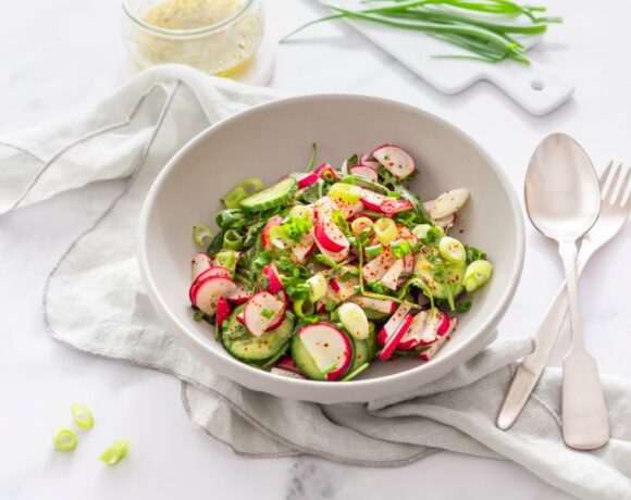 White bowl on a white background filled with a salad composed of radish, cucumber and green onions.
