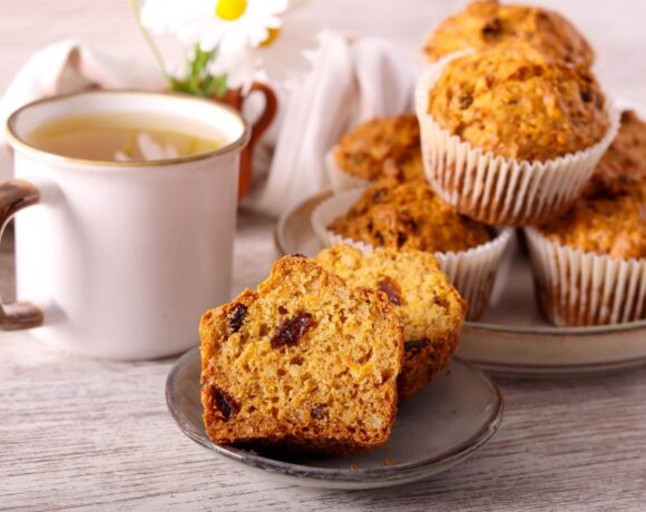 Carrot raisin muffin sliced in half and presented on gray plate with mug of hot tea in background.