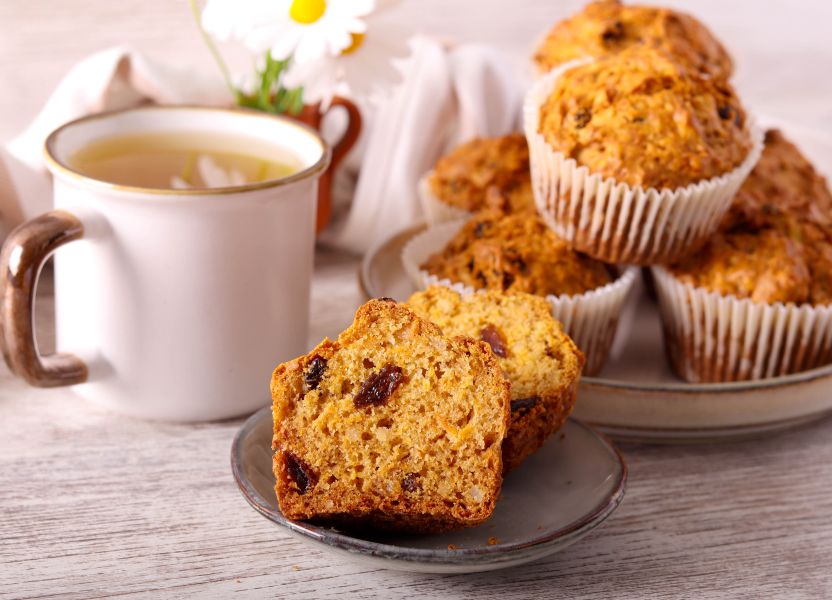 Carrot raisin muffin sliced in half and presented on gray plate with mug of hot tea in background.