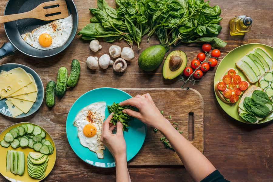 Overhead shot of hands preparing a meal over cutting boards with fresh produce and eggs in the shot
