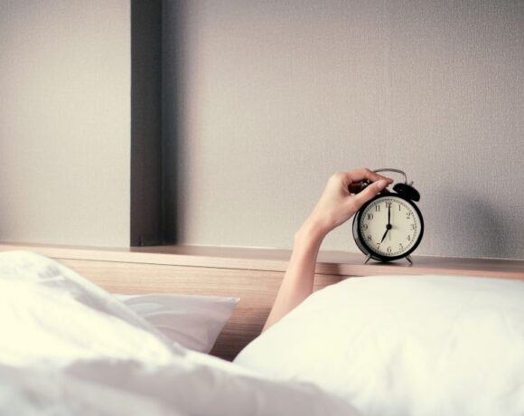 hand emerging from blankets touching an alarm clock