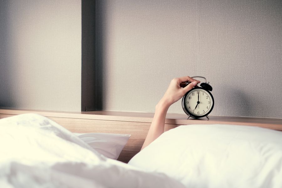 hand emerging from blankets touching an alarm clock